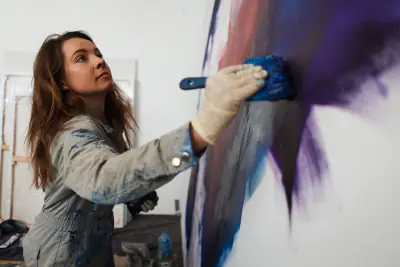 Rebecca Gischel trägt Farbe mit dem Pinsel hoch an der Leinwand auf
