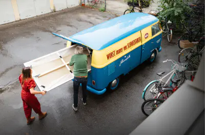 Rebecca Gischel und Karl Schweisfurth verladen ein Gemälde in einen historischen Herrmannsdorfer Lieferwagen
